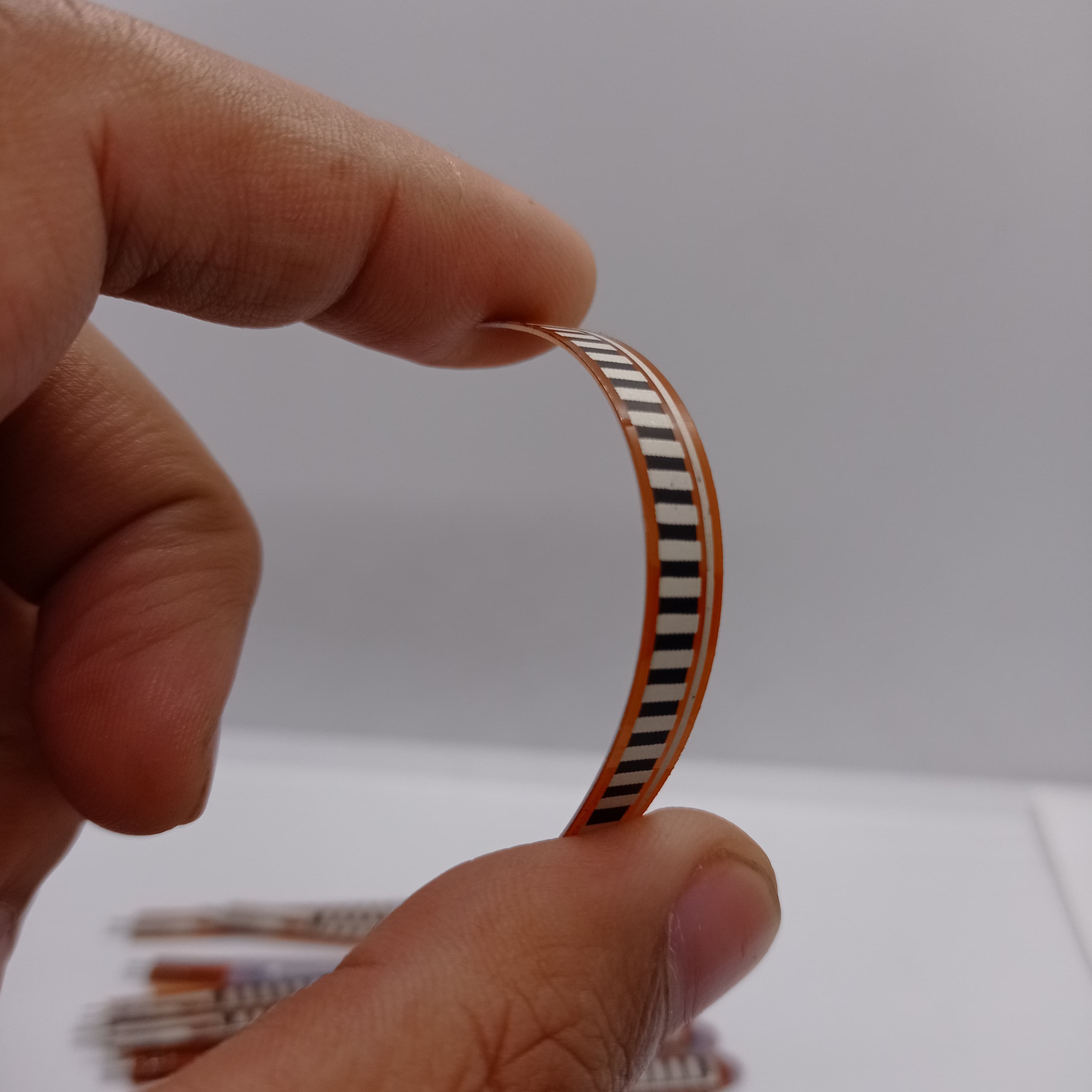 1 Piece 2.2 Inch Flex Sensor Bend Detection Sensor - a thin, orange, flexible strip with black and white striped segments being held between a thumb and index finger.