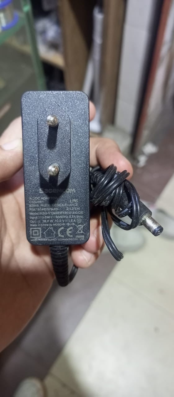 12V 1.5A Power Supply Adapter With Power Indication | Stock Lot - a black wall-plug power brick with an attached DC barrel connector cable, held in a hand showing the printed specifications.