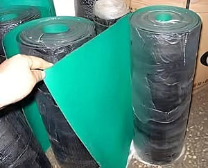 1m*1m*2mm Antistatic ESD Floor Mat/ESD Rubber Table Mat For Production/S5 PVC Antistatic Workbench Rubber Mat - a hand unrolling a section of the green and black rubber mat from a large, plastic-wrapped roll.