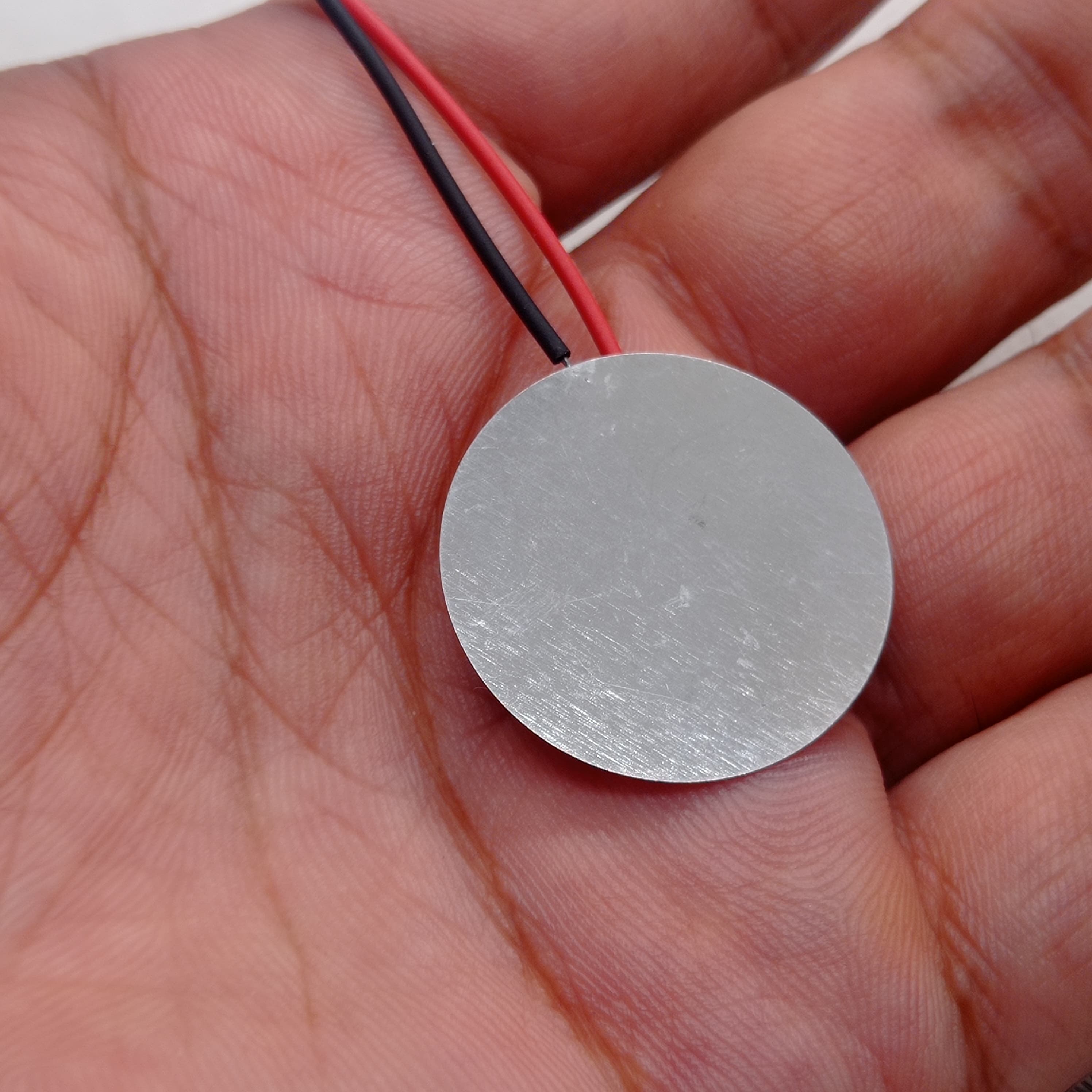 27mm Piezoelectric Ceramic Disc Piezo Element Plate With Wires - shown as a silver circular metal disc held in a hand with attached red and black wires.