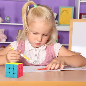 3 By 3 Rubik Cube 3x3 - shown as a multi-colored cube with yellow, blue, and red faces sitting on a desk next to a young girl drawing in a notebook.