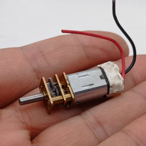 300RPM N20 DC Gear Motor The Perfect Low RPM High Torque Motor For Your Electronics Projects - held in a hand, showing a silver metal motor body, a brass gearbox with exposed gears, a metal output shaft, and two wires.