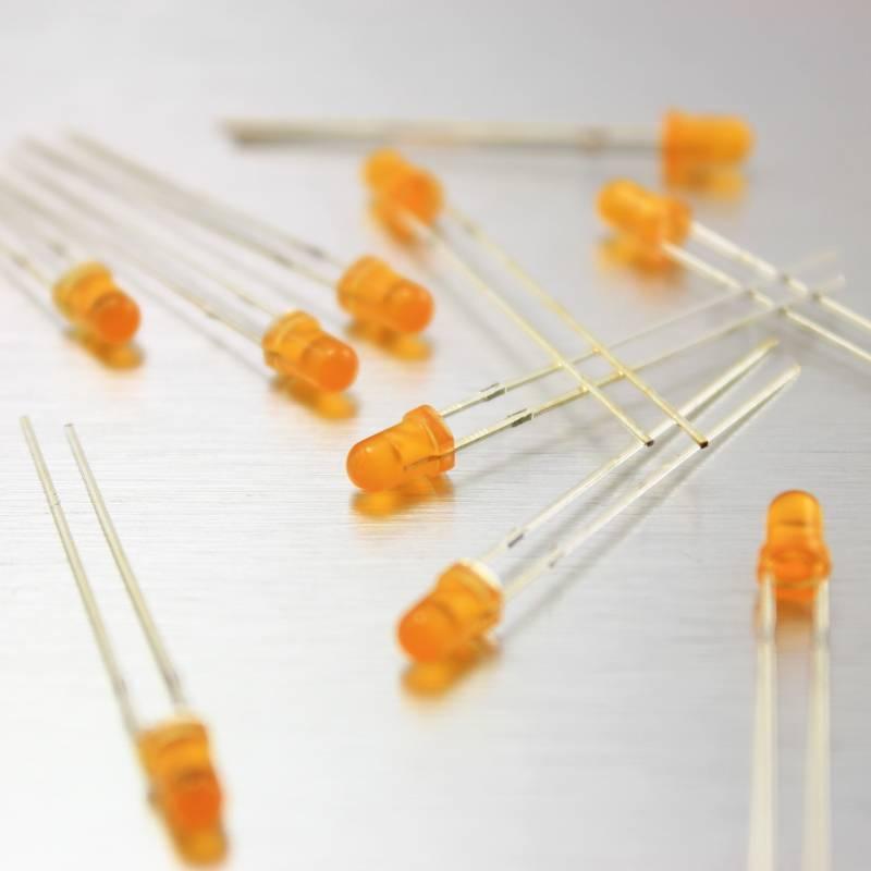 3mm Orange LED - a scattered collection of small, round, orange-coloured light-emitting diodes with two metal leads each on a metallic surface.
