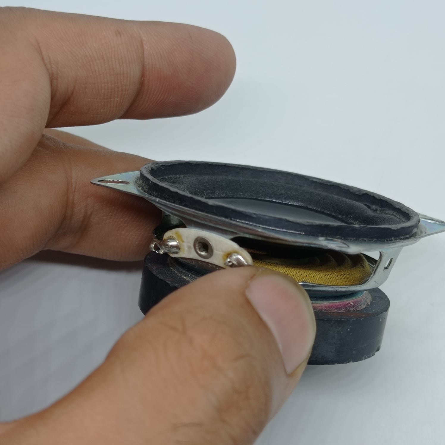 4 Ohm 5 Watt Speaker - shown in a close-up view held by fingers, featuring a circular black speaker cone with a metallic frame and two solder terminals.
