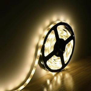 5m 5050 SMD 300 LED Warm White Waterproof Strip Lighting 12V Flexible - coiled on a black plastic spool and illuminated against a wall.