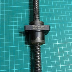CNC Ball Screw - a black metal screw shaft with a THK branded nut assembly featuring the text KX04 H06514, resting on a green cutting mat.