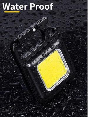 COB Rechargeable Keychain Flashlight | Mini Small Flashlight With 3 Light Modes, Folding Bracket, Bottle Opener, And Magnet Base For Fishing, Walking, - a black square-shaped light with a central yellow panel, integrated carabiner, and bottle opener on a wet surface.
