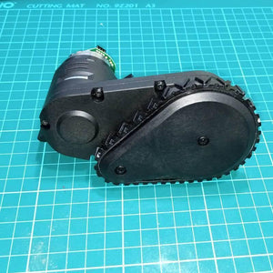 DC Gear Motor With Encoder With Wheel - black motor assembly with an attached encoder circuit board and a black plastic wheel, resting on a green mat.