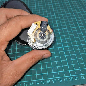 DC Gear Motor With Encoder With Wheel - close-up of the circular encoder disc, circuit board, white connector, and black optical sensor held by a hand.
