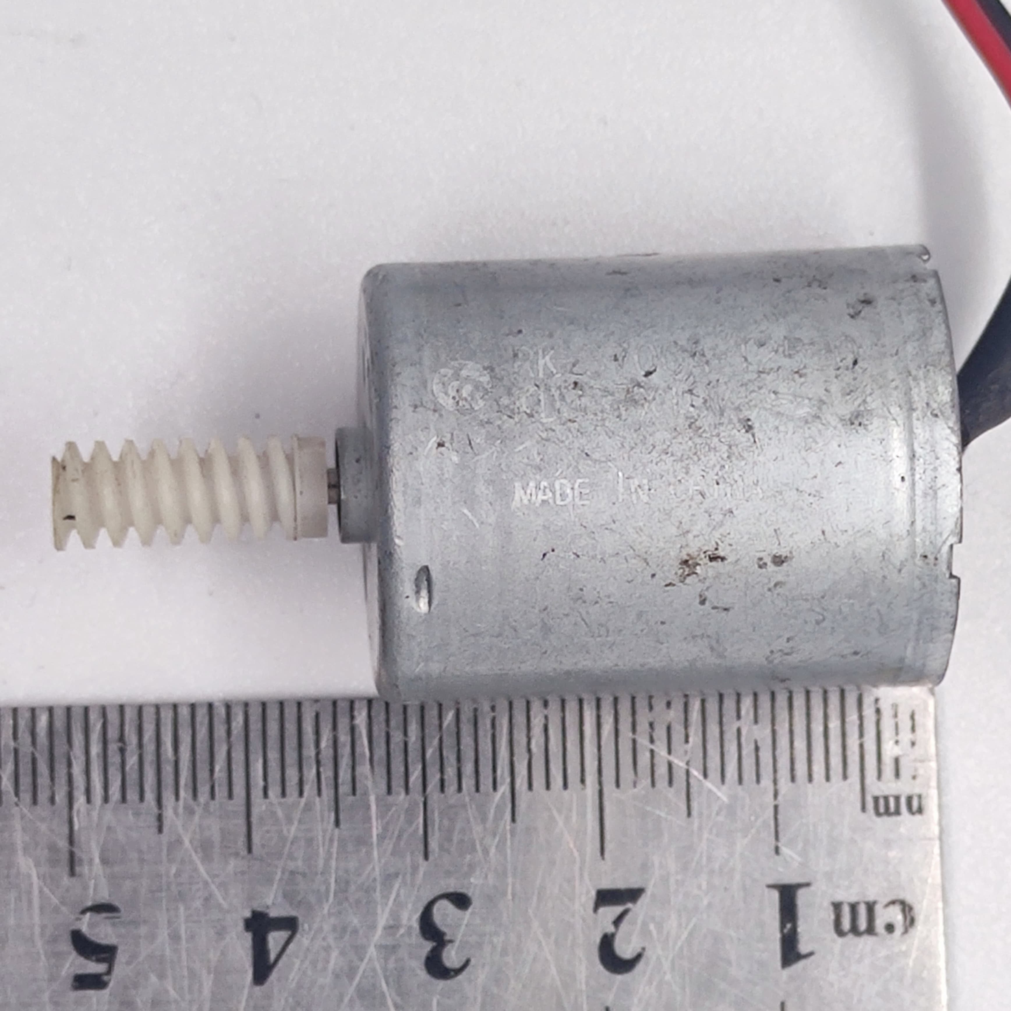 DIY Mini 5vdc DC Motor - shown next to a metal ruler to indicate its size, featuring a silver cylindrical body and a white plastic worm gear on the shaft.