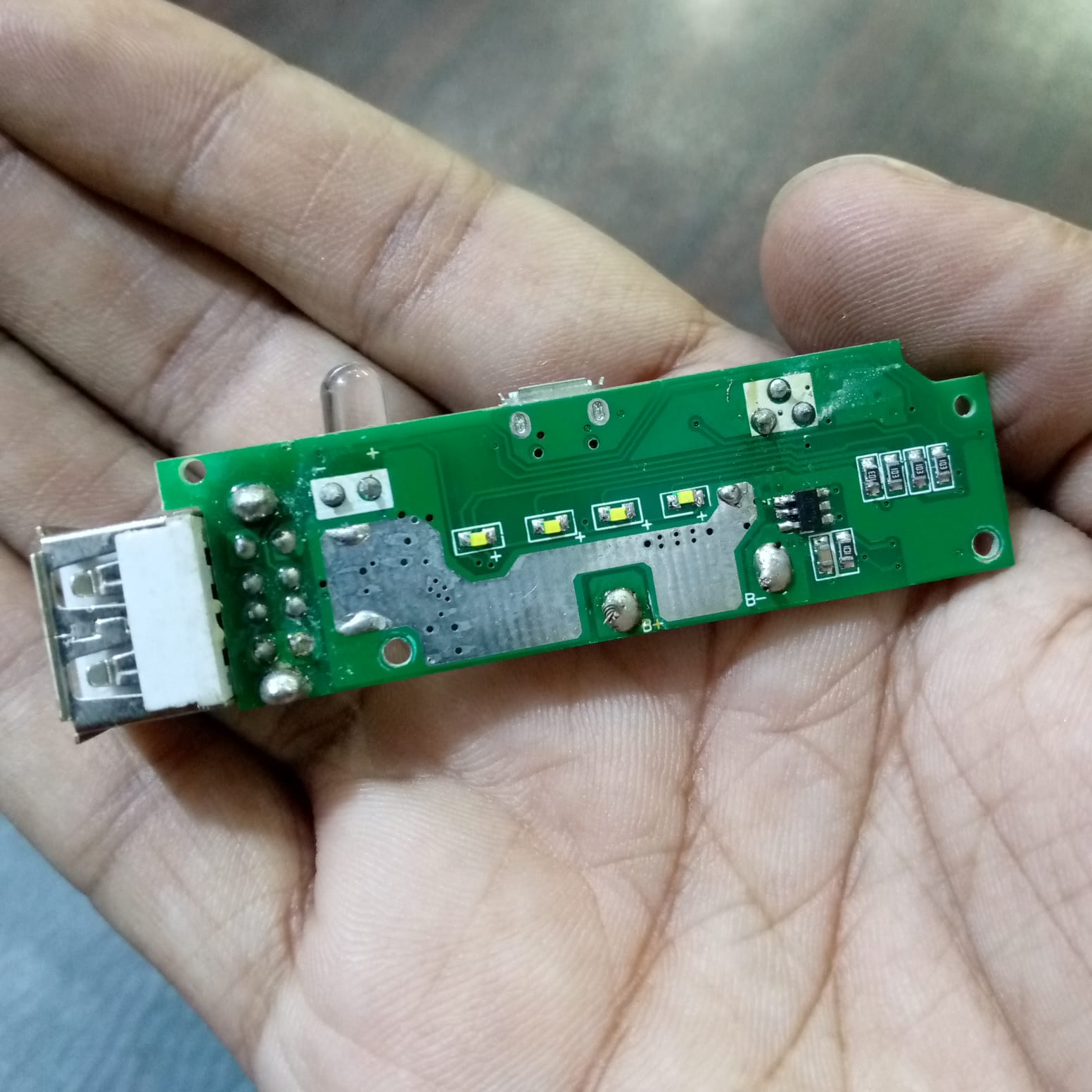 Dual USB Power Bank Module - shown as a green rectangular circuit board held in a hand, featuring a USB-A port, a micro-USB port, and four LEDs.