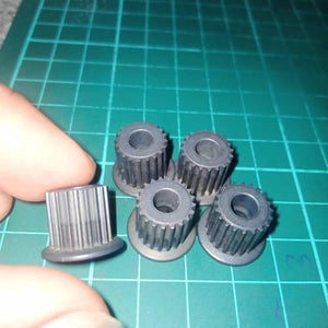 Japanese GT2 20 Teeth 5mm Bore Push Fit Pulley Timing Pulley - a close-up of five grey, cylindrical, toothed pulleys on a green cutting mat.