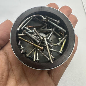 Magnet for storing screws and metal - a circular black magnetic tray held in a hand filled with various assorted metal screws.