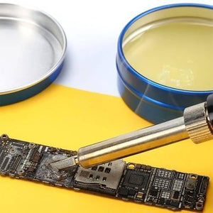 Mechanic Soldering Flux Paste PCB BGA Welding Flux Gel Tin MCN-UV50 - shown in a blue tin container with its lid nearby, while a soldering iron tip works on a small circuit board.