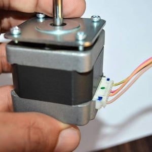 NEMA17 NEMA 17 Stepper Motor For 3D Printer And CNC - a close-up of the silver and black square motor held by a hand with a white 6-pin connector attached.