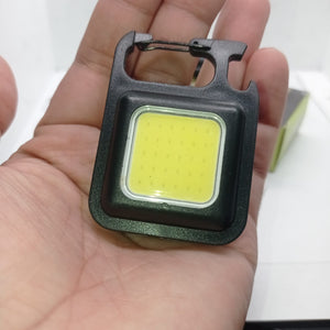 Portable COB Flashlight - Emergency Light with Rechargeable Keychain - Durable Plastic Casing - a black square-shaped rechargeable keychain light with a COB LED panel and integrated carabiner held in a hand.