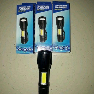 Portable Mini Telescopic Zoom Xpe COB LED Main Light White Light - one black flashlight placed in front of three identical retail boxes on a speckled surface.