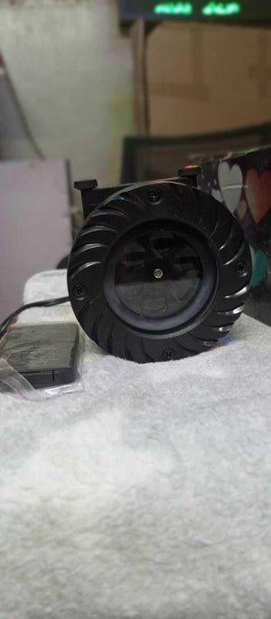 Projector - with a round black housing featuring a spiral-patterned bezel, a central lens, and an attached black power cable with a small control box.