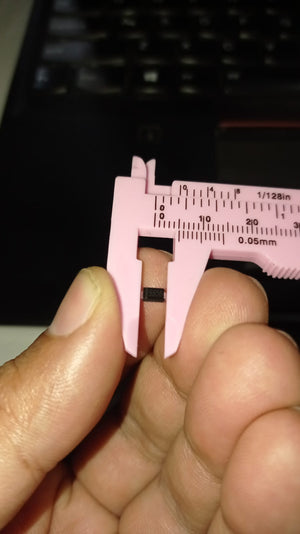 SS56 SMD 5A 60V DO-214AA Schottky Diode - held between the jaws of a pink plastic vernier caliper, showing a close-up of the component's size.