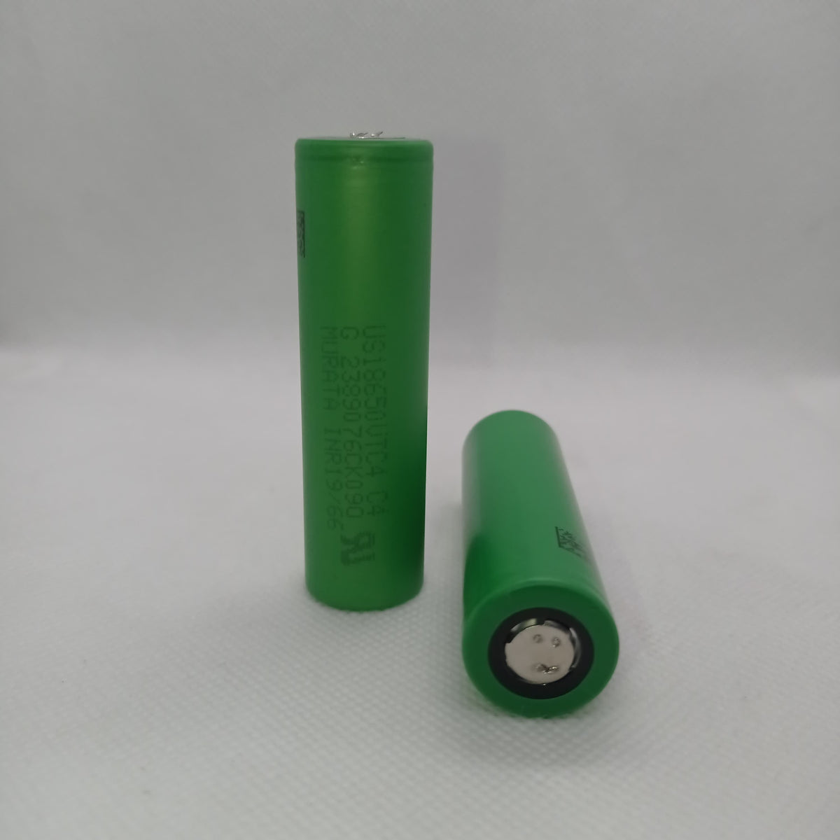 Stock Lot US18650UTC4 3.7V 2000mA 18650 Li-ion Rechargeable Battery – High-Capacity Power Cell for Flashlights, Laptops, and Power Tool - two green cylindrical cells shown with one standing upright and one lying horizontally on a white surface.
