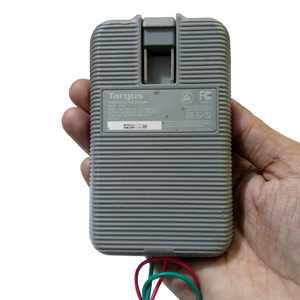 Targus Apa Power Supply 24V 4.75A - shown as a grey, rectangular, ribbed-textured charger held in a hand with exposed green and red wires at the bottom.