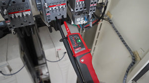 UNI-T UT15B Waterproof Voltage & Continuity Tester Pen – AC/DC up to 690V, Three-Phase Rotation, IP65, Single-Probe Live Wire Detection with Work Light - and black handheld device with a lit LED display, testing electrical connections on an ABB contactor in a control panel.