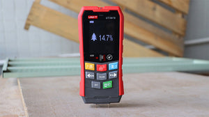 UNI-T UT387S Wall Scanner – Metal to 100 mm, Live AC Wire to 40 mm, 40 m Laser Distance, Wood Moisture 6~40%, 2.4in Colour Screen, Voice Broadcast - a red and grey handheld device with a color screen showing a tree icon and 14.7% reading, standing on a wooden surface.