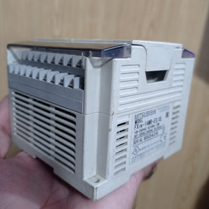 Used Mitsubishi PLC Fx1n-14MR-ES/UL - a beige, rectangular industrial controller held in a hand, showing its side label, screw terminals, and ventilation slots.