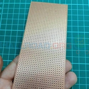 Veroboard Dotted Small Stripboard 6.5x14.5cm - a rectangular copper-colored circuit board with a grid of holes held in a hand over a green cutting mat.
