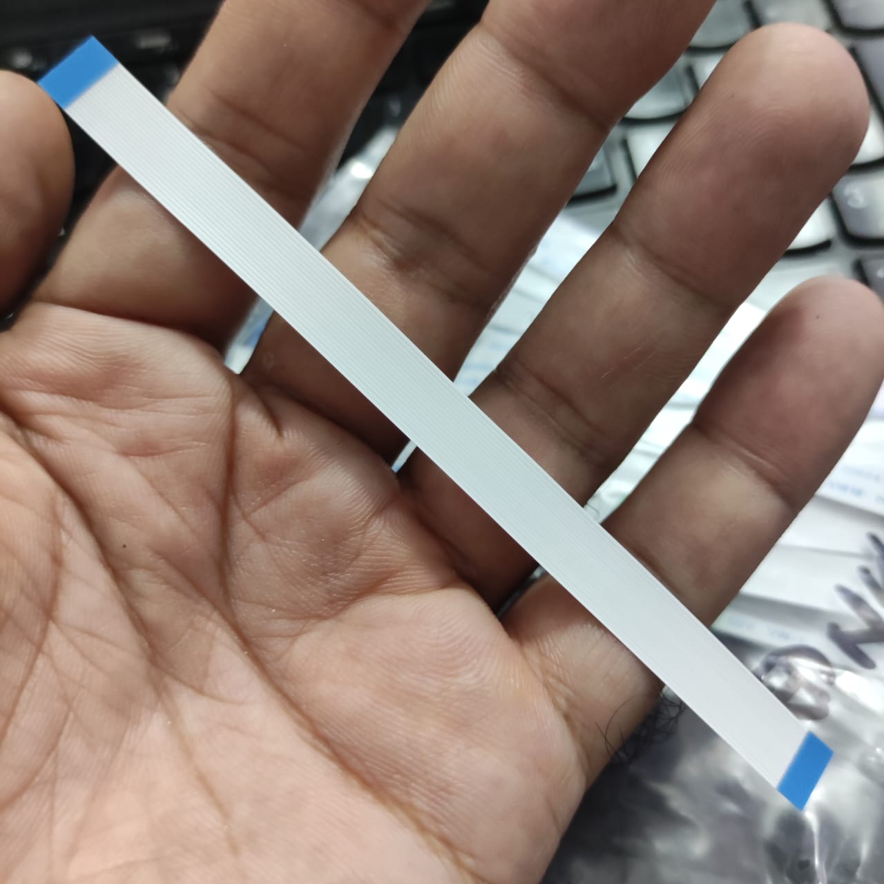 0.5-16P-120mm 0.5 Inch Pitch 16 Pin 120mm Leght Ffc Flexible Flat Cable - shown as a long, thin, white ribbon cable with blue reinforcement tape on both ends, held in a person's palm.