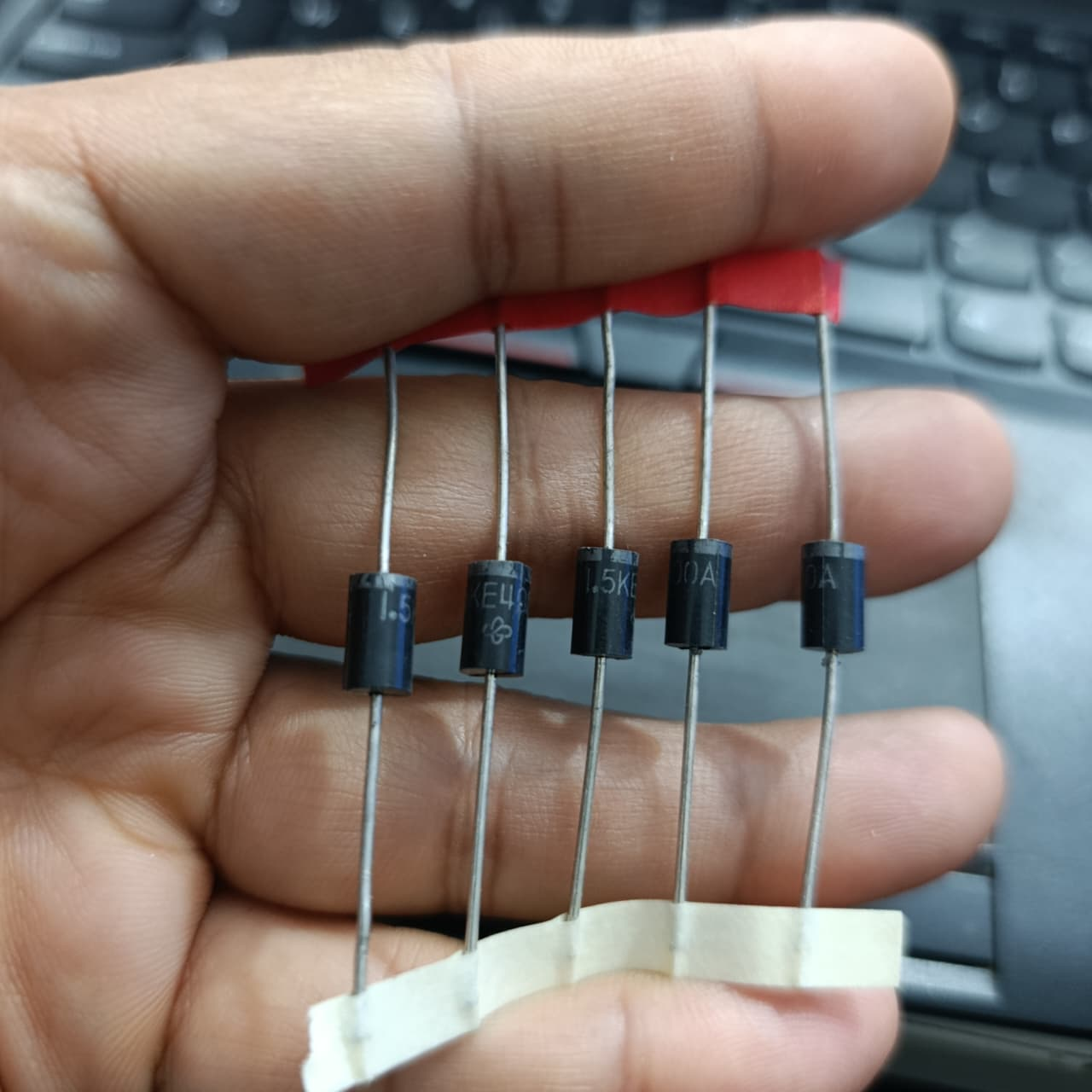 1.5KE400A TVS Diode – 1500W Transient Voltage Suppressor 400V Unidirectional - five black cylindrical electronic components with metal leads held in a hand, showing printed text on their bodies.