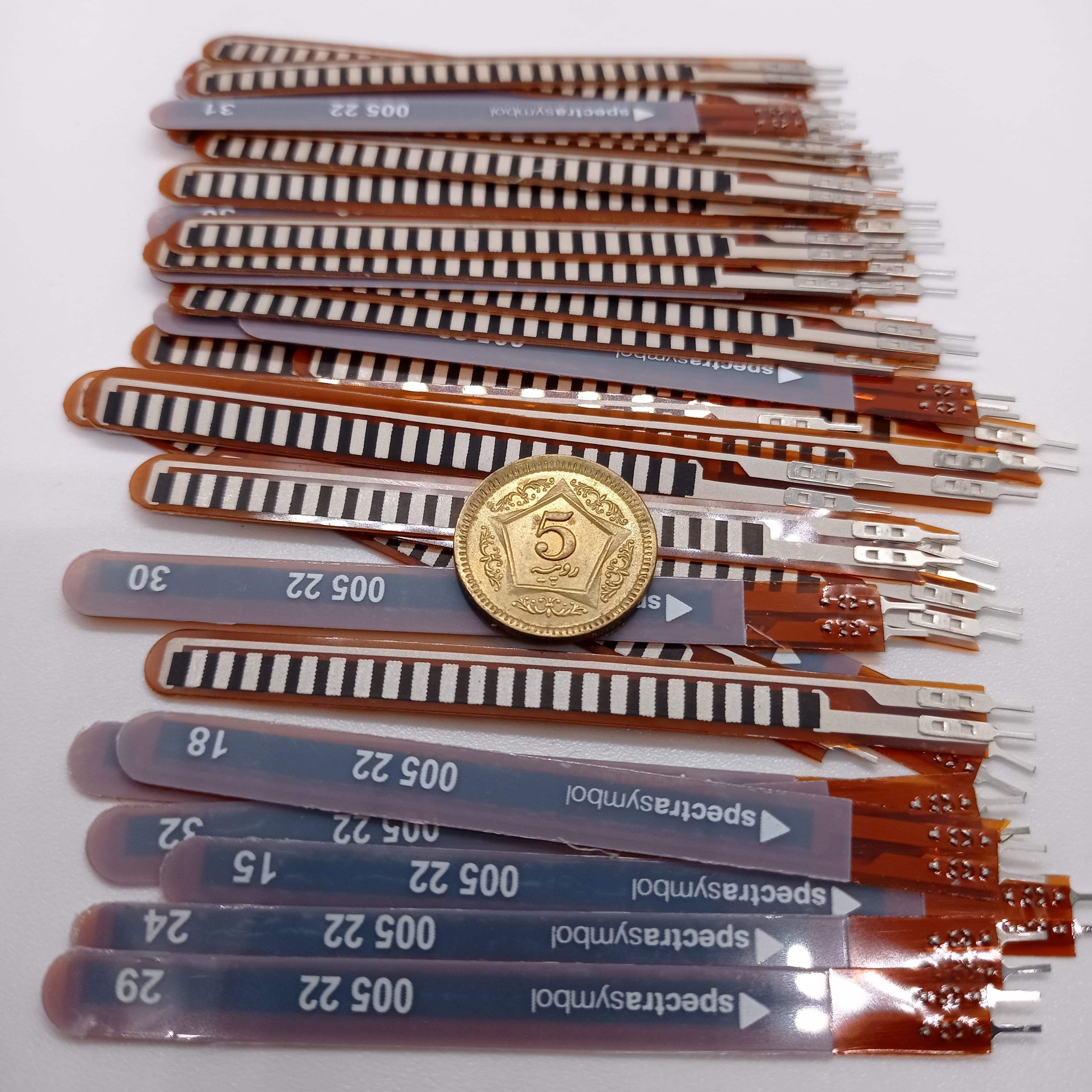 1 Piece 2.2 Inch Flex Sensor Bend Detection Sensor - shown as a pile of thin, brown, rectangular flexible strips with a gold-coloured coin on top.