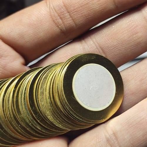 1 Piece 27mm Piezoelectric Transducers Piezoelectric Sensor , Piezo Transducer - a close-up shot of a single round brass-colored sensor with a central white ceramic disc held in a hand.