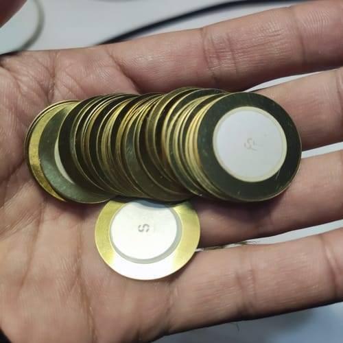 1 Piece 27mm Piezoelectric Transducers Piezoelectric Sensor , Piezo Transducer - a hand holding a stack of circular gold-coloured metal discs with white ceramic centers.