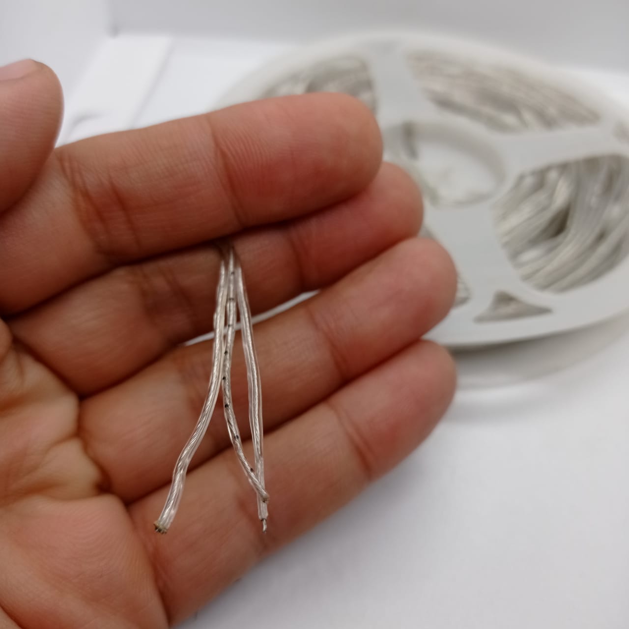 1 Piece RGB Waterproof WS2812 Addressable LED Strip For Arduino (individually Controllable!) - close-up of a hand holding the stripped wire ends of a coiled, transparent LED strip.