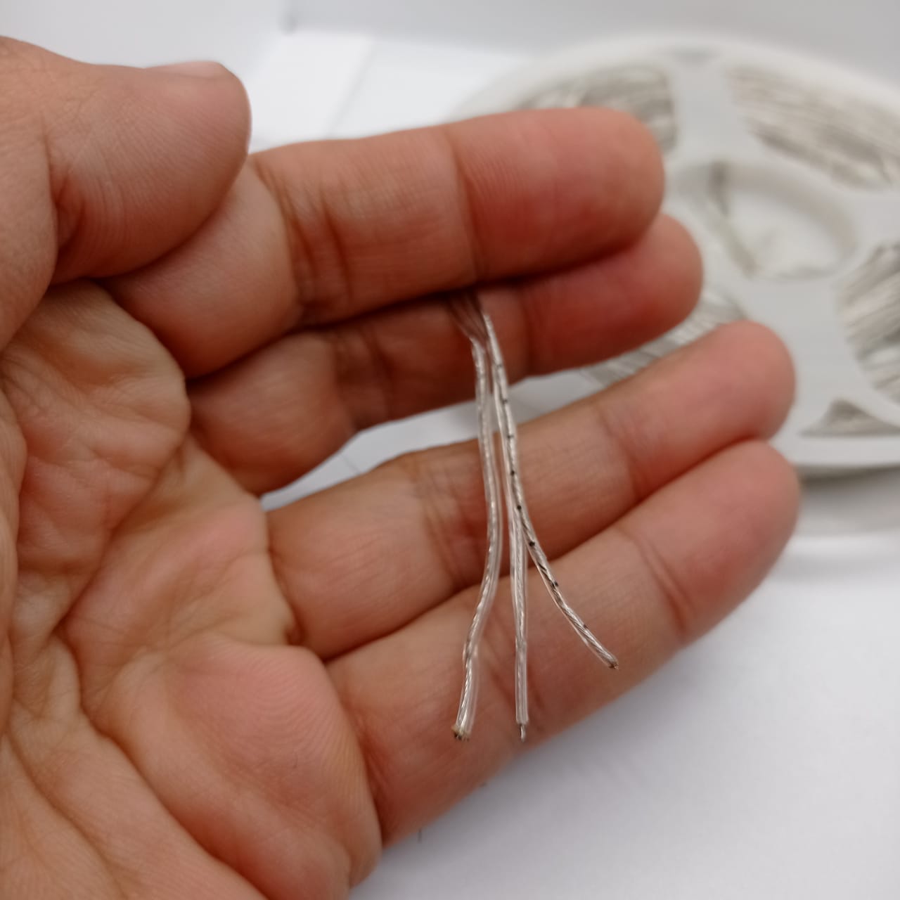 1 Piece RGB Waterproof WS2812 Addressable LED Strip For Arduino (individually Controllable!) - close-up of three thin, transparent, multi-strand wires held in a hand with a spool in the back.