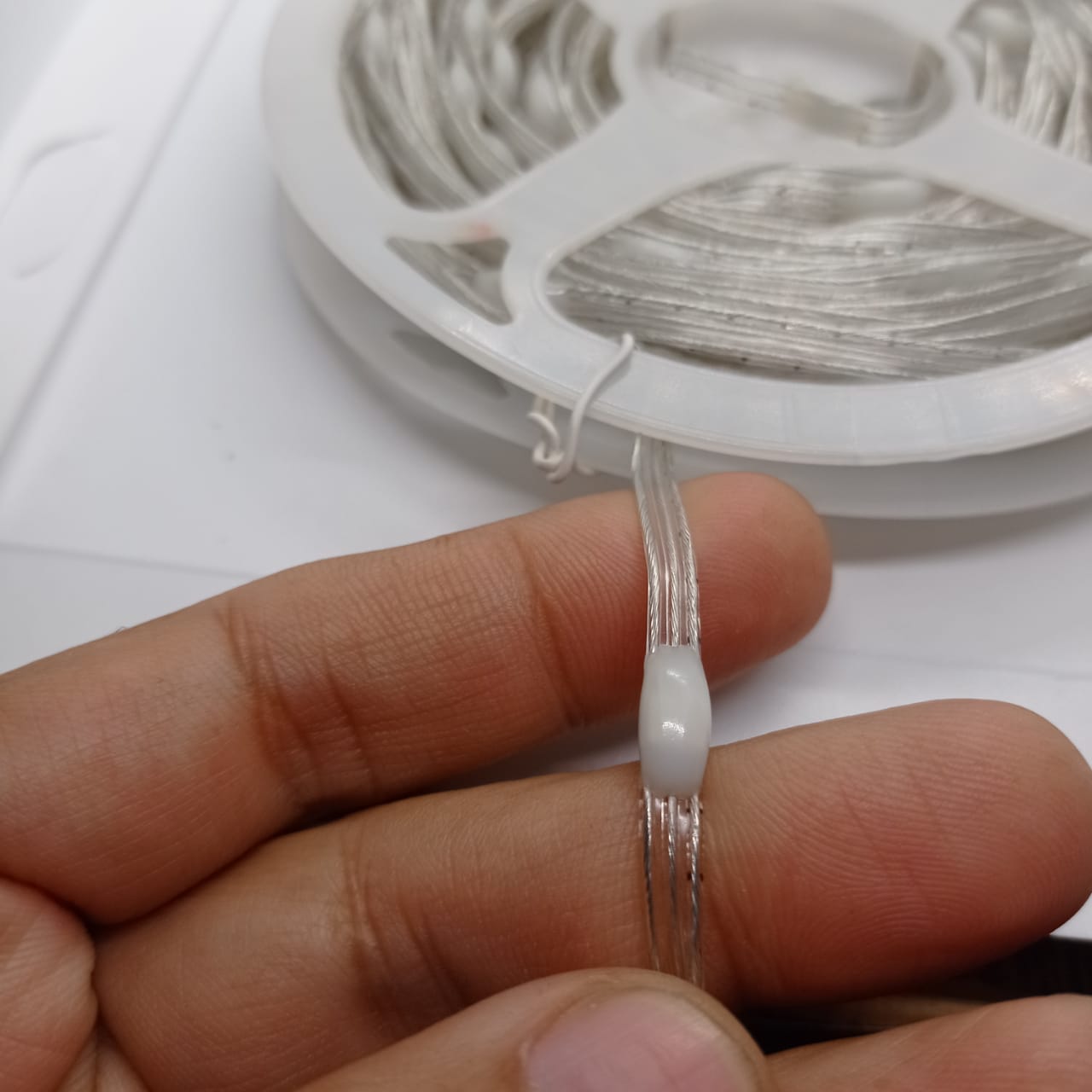 1 Piece RGB Waterproof WS2812 Addressable LED Strip For Arduino (individually Controllable!) - shown as a close-up of the wire held in a hand with the strip coiled on a plastic spool.