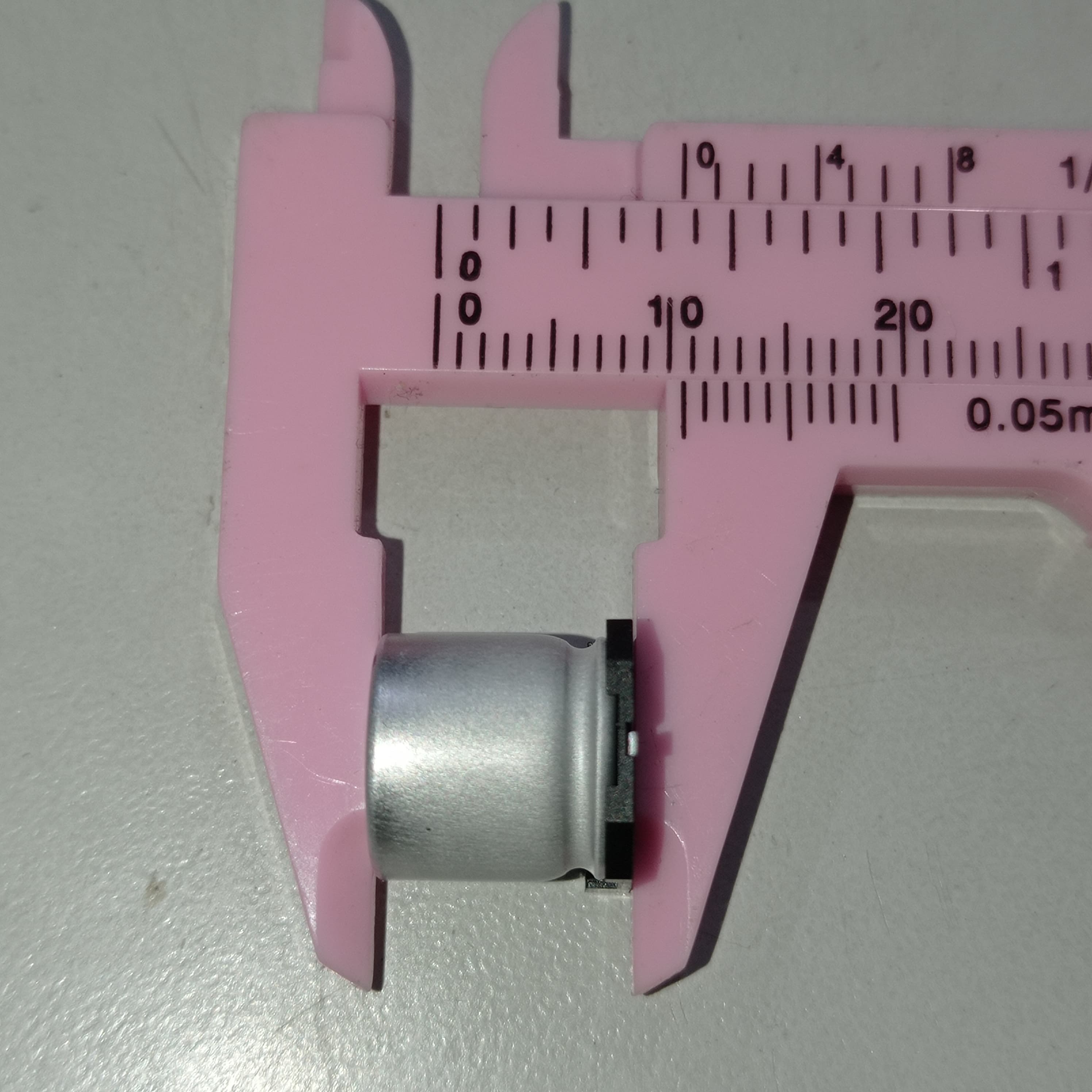 1000uF 16V SMD Capacitor D10XL10.2mm Aluminum Electrolytic Capacitors - SMD - shown in a close-up view being measured by pink plastic digital calipers indicating a width of approximately 10mm.