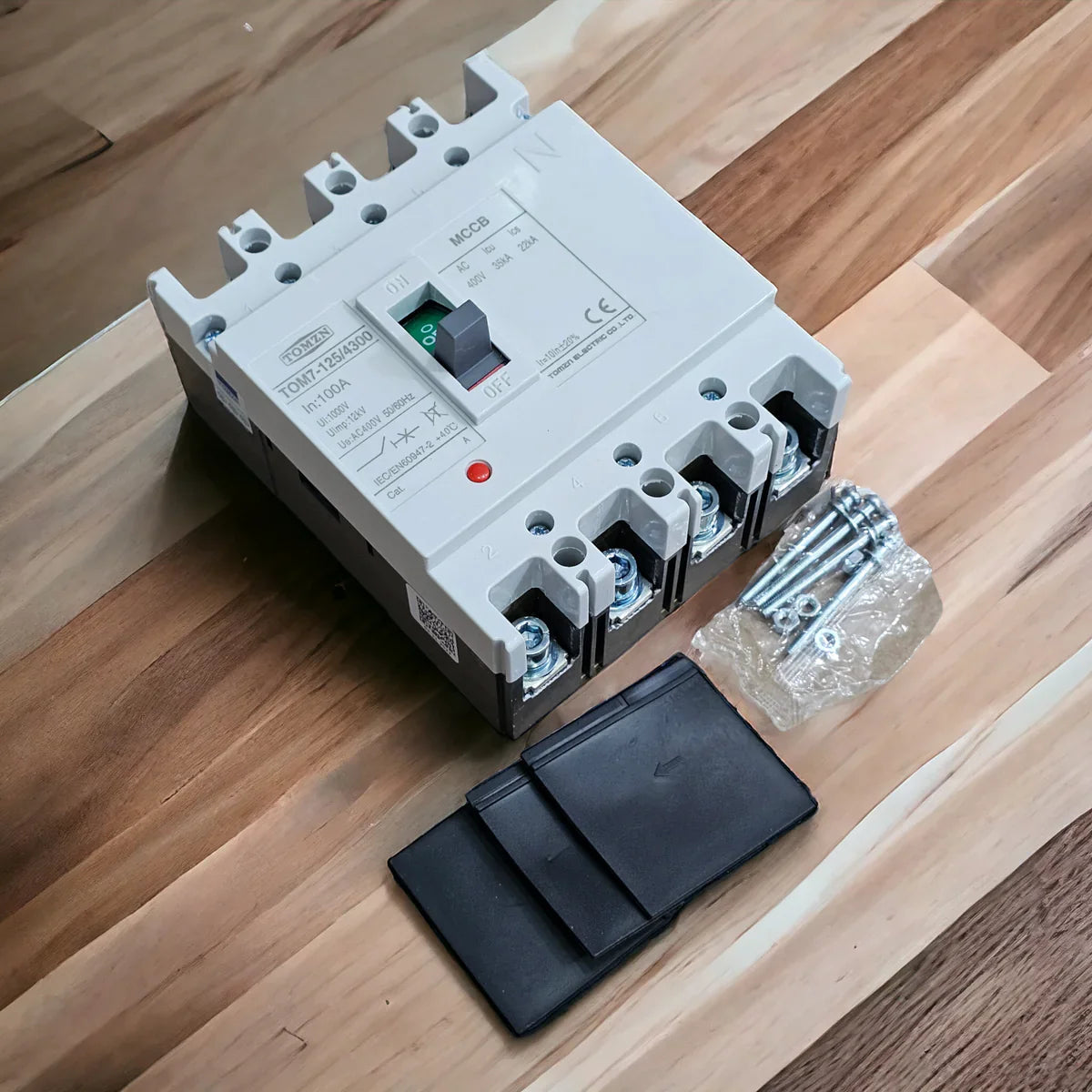 100A Tomzn TOM7-125/4300 Mccb 100A 4 Pole Circuit Breaker - with a grey casing, a central toggle switch, terminal screws in a plastic bag, and a black cover.