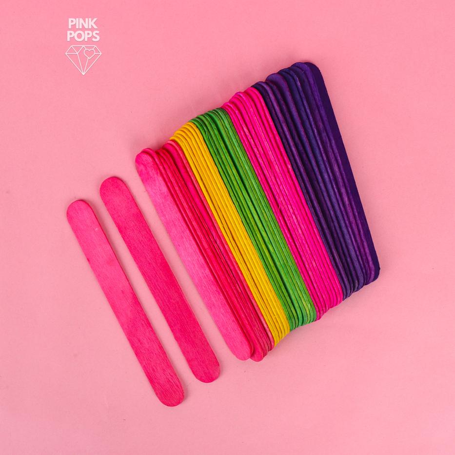 100pcs popsicle stick mix colour ice cream sticks - shown as a stack of flat, wooden sticks in pink, yellow, green, and purple on a pink background.