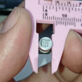 100uF 16V ±20% SMD D6.3XL5.4mm Aluminum Electrolytic Capacitor - shown in a close-up being measured by pink plastic calipers, with "X4460 100 16D" printed on its top.