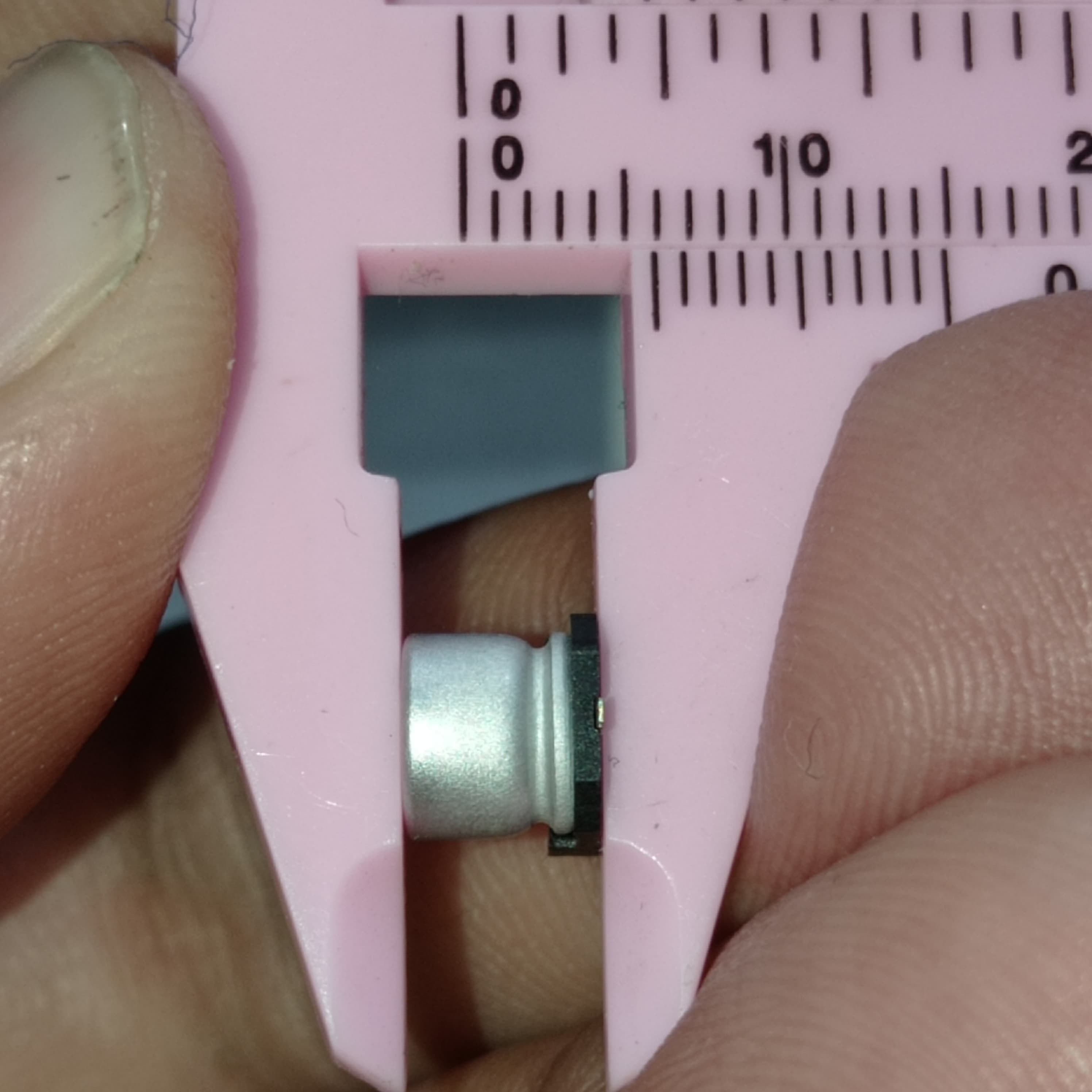100uF 16V ±20% SMD D6.3XL5.4mm Aluminum Electrolytic Capacitor - a silver cylindrical component held in pink plastic calipers showing its physical dimensions.