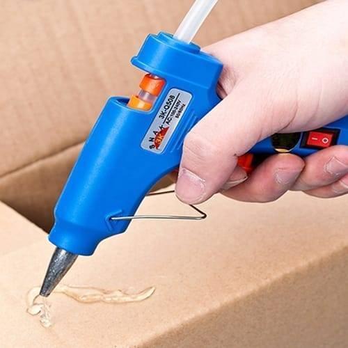 11mm Hot Melt Glue Sticks Electric Heating Adhesive Film Craft Glue Stick - shown as a blue glue gun being held and used to apply adhesive to cardboard.