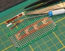 12mm One Sided Copper Foil Conductive Adhesive Tape - shown as strips applied to a green breadboard alongside tweezers and a small screwdriver.