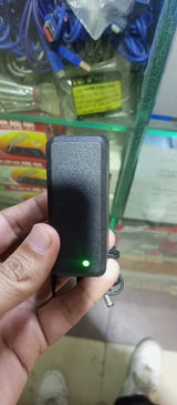 12V 1.5A Power Supply Adapter With Power Indication | Stock Lot - a black rectangular power brick held in a hand, featuring a glowing green power indicator light.