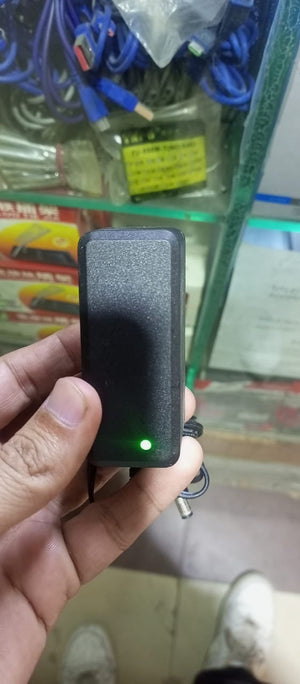 12V 1.5A Power Supply Adapter With Power Indication | Stock Lot - a black rectangular power brick held in a hand, featuring a glowing green power indicator light.