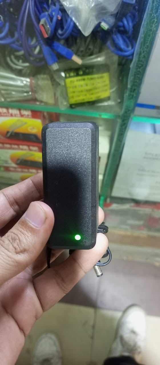 12V 1.5A Power Supply Adapter With Power Indication | Stock Lot - a black rectangular power brick held in a hand, featuring a glowing green power indicator light.