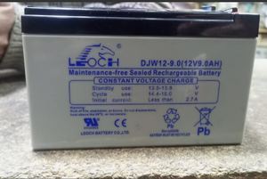 12V 9A DC Battery - shown as a rectangular, grey Leoch DJW12-9.0 lead-acid battery with black top terminals and printed technical specifications.