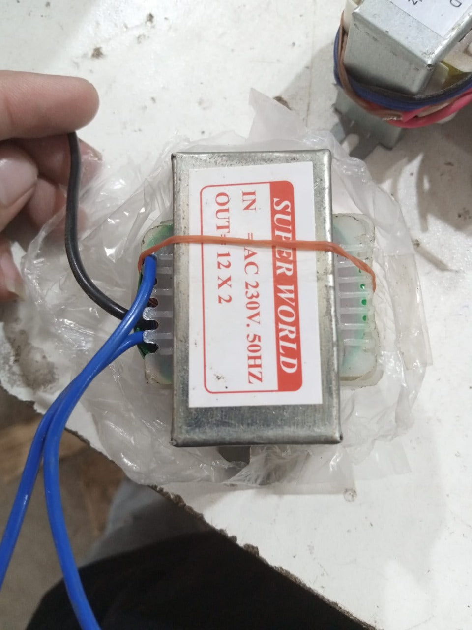 12V + 12V 2A Transformer 24V 2A Transformer - shown as a metal-cased component with blue and black wires, wrapped in clear plastic on a white surface.