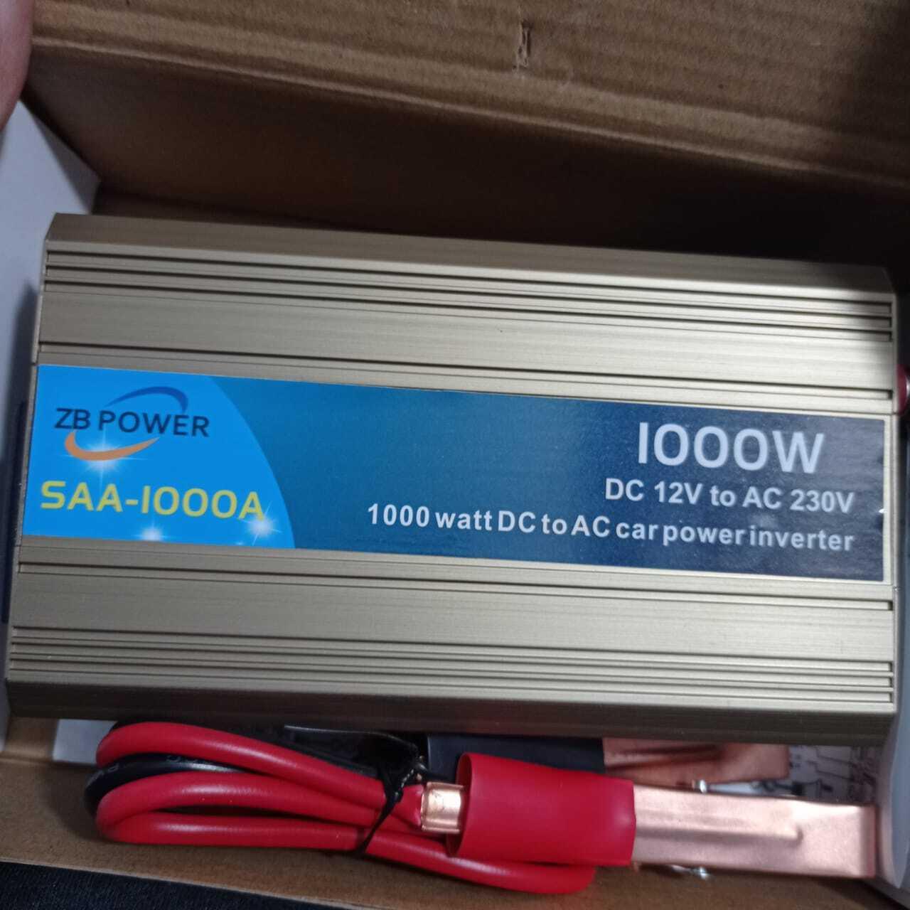 12V To 220V 1000W Power Inverter Car Power Inverter - shown in its box with a gold-toned metal casing, blue label, and red and black battery clamp cables.